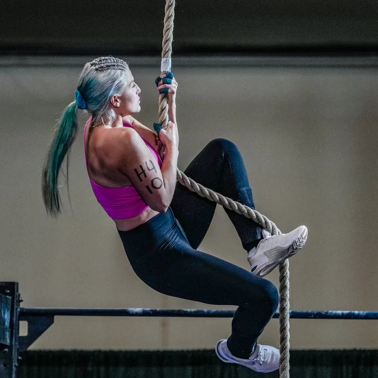 A CrossFit competitor climbing up a rope in a gym.