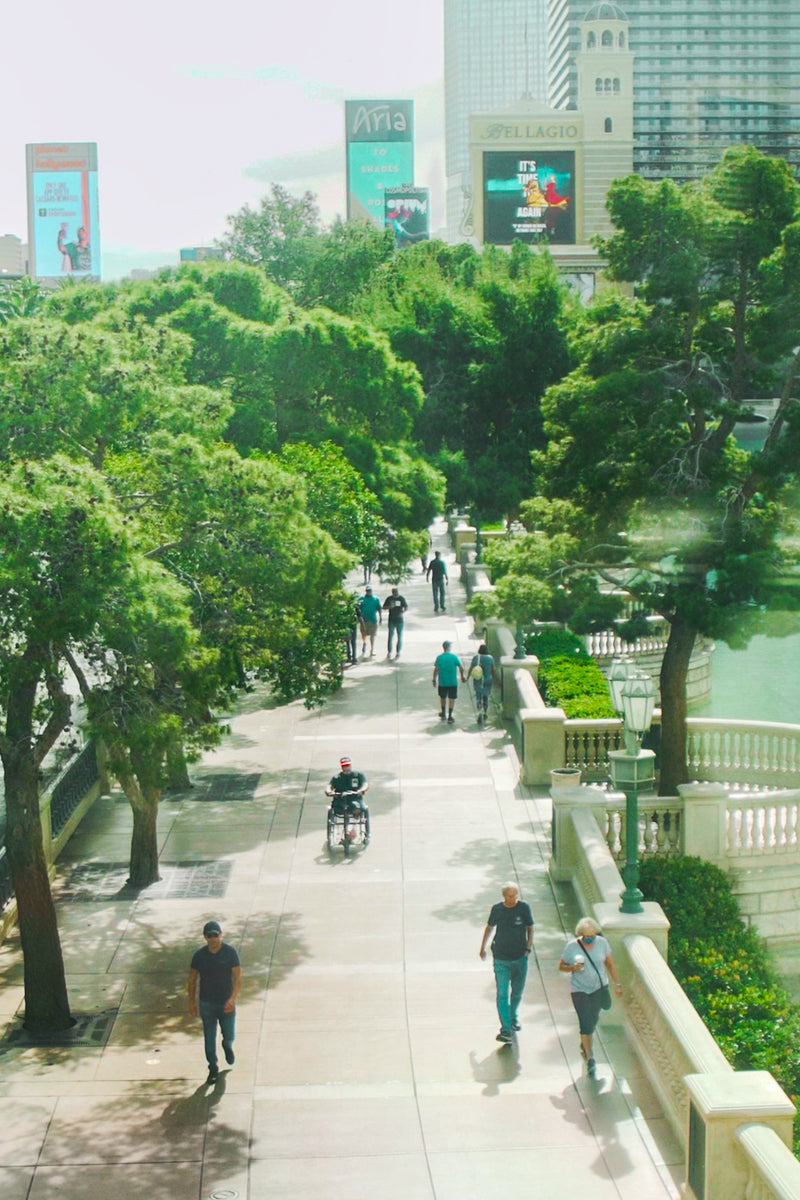 Wide photo of the Bellagio walkway on the Las Vegas Strip with Amplife® Foundation & Amplife® Founder Abdul Nevarez riding his Rio Mobility Firefly 2.5 Electric Scooter Wheelchair Attachment