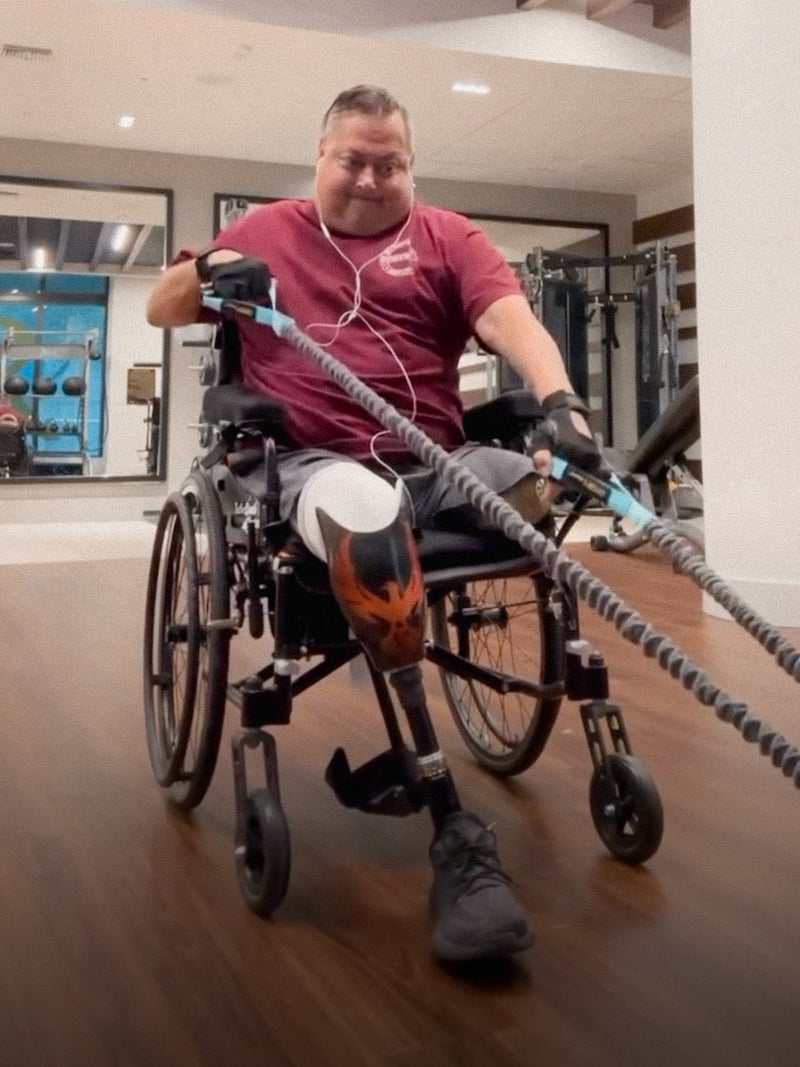 Team Amplife® Ambassador Bert Chirino in the gym performing cable rows in his wheelchair and rockin’ his Amplife® while wearing the Severed Society® Members Only T-Shirt and Death Cheater™ Halo Sticker on the side of his wheelchair