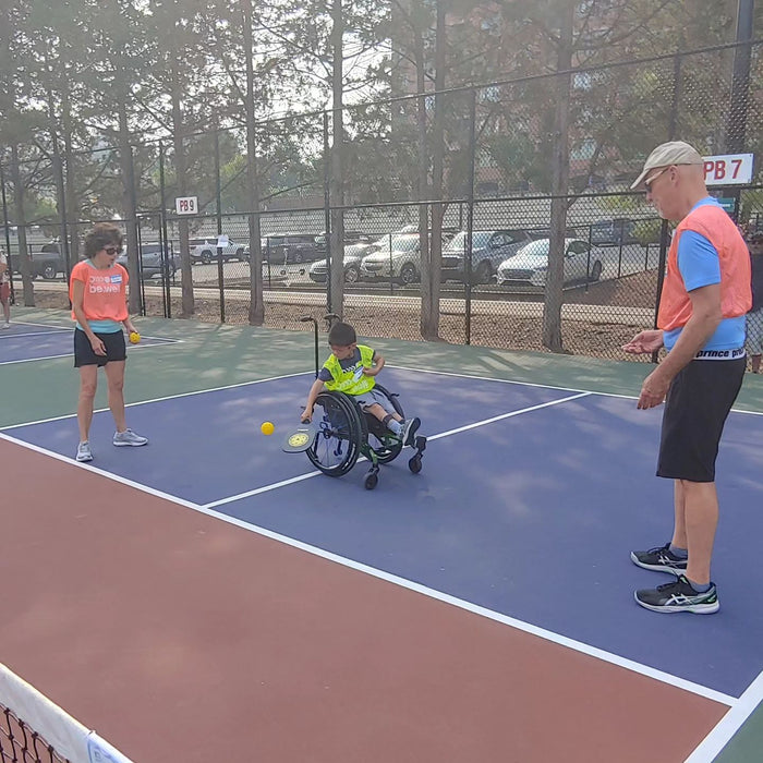 Cincinnati Tennis Foundation Coaches with pickleball participant returning a serve in their wheelchair.