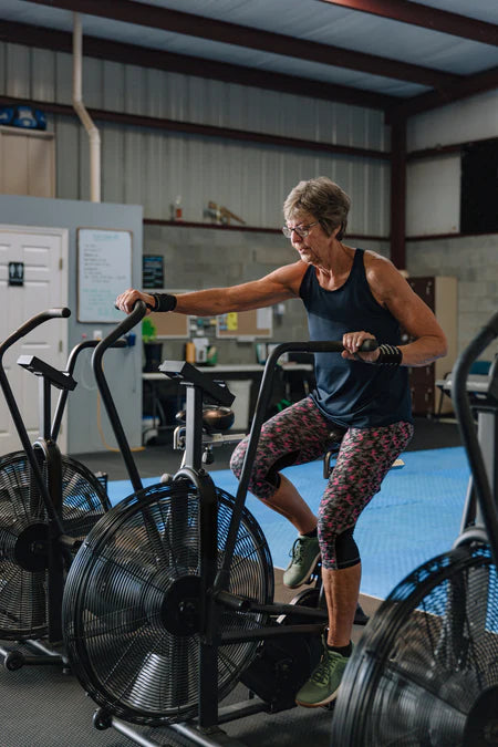 Older lady using an Assault Bike in a CrossFit Gym.