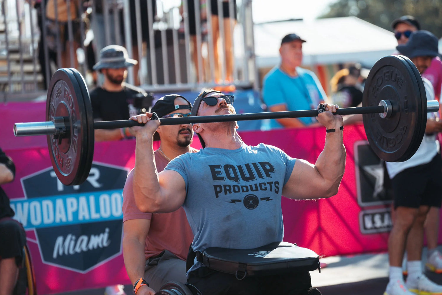 A double above the knee amputee in a competition shoulder pressing a barbell with 20lbs on each side and the LapMat™ ready to hold the bar once the exercise is completed.