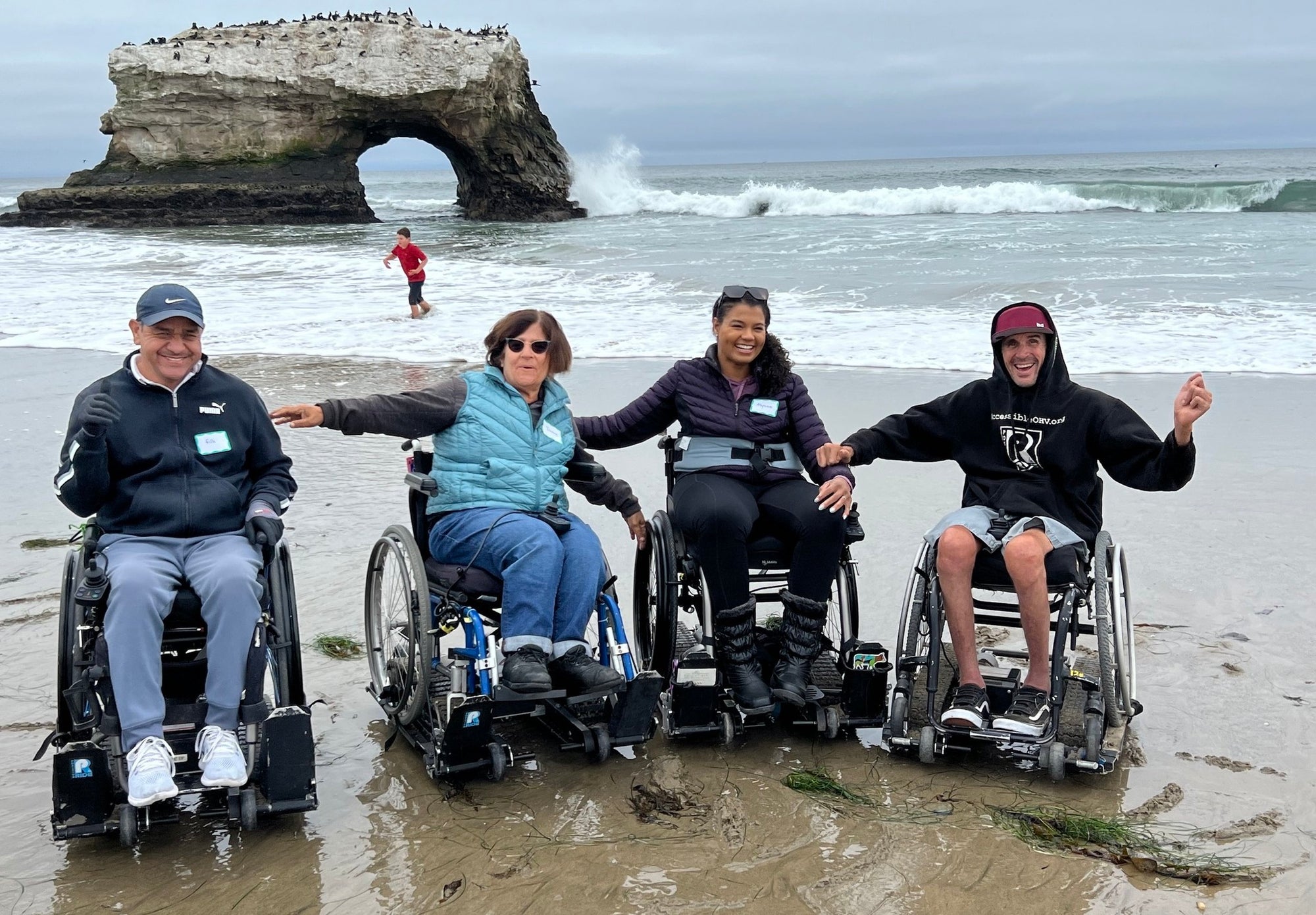 Group of NorCal SCI members on the beach in their wheelchairs on an attachment that rolls on sand.