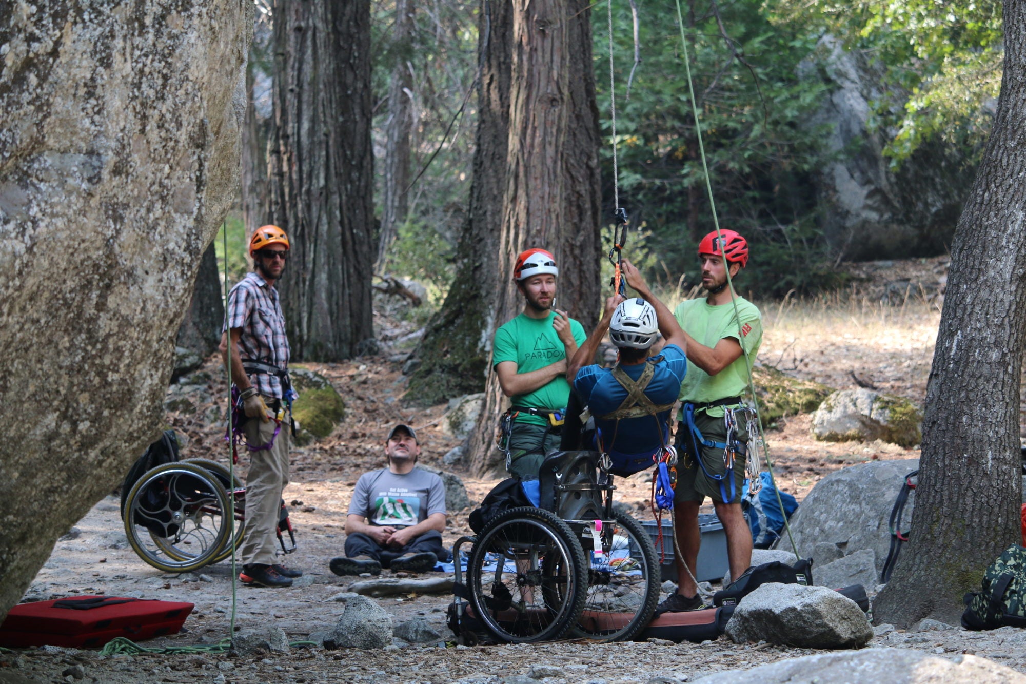 Paradox Sports participants watching as a fellow climber is being hoisted from their wheelchair to begin their climb.