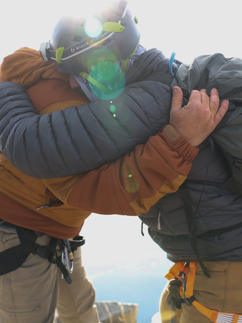 Two climbers hugging at the peak of a mountain.