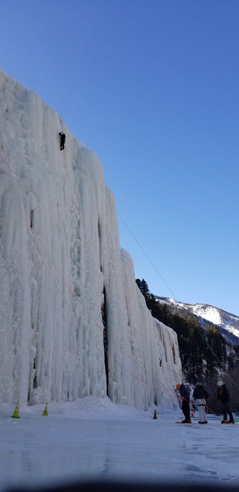 Paradox Sports climber ascending the icewall at the Lake City Ice Skills 201 with a line of climbers at the base.