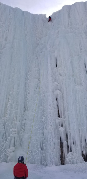 A Paradox Sports climber ascending the icewall with a climber watching at the base of the Lake City Ice Skills 201.