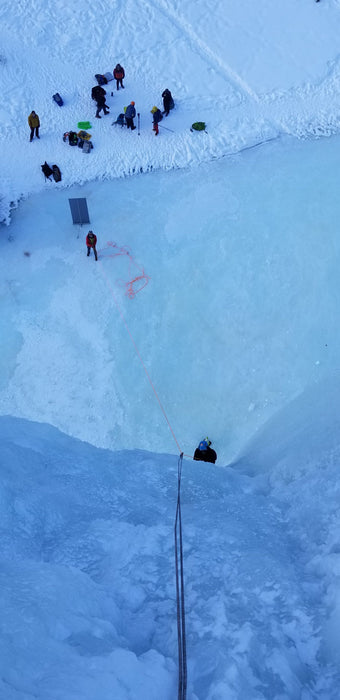 Top of the icewall with a Paradox Sports climber ascending and a group of climbers at the base of the Lake City Ice Skills 201.