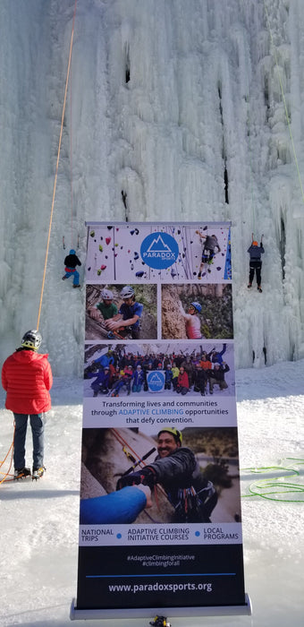 Paradox Sports banner at the base of the Lake City Ice Skills 201 with Paradox Sports climbers ascending the icewall.