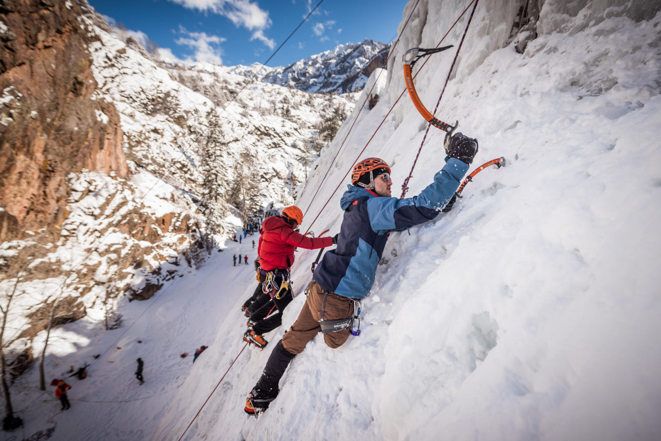 A Paradox Sports climber about to put their ice pick into the icewall with a group of Paradox Sports climbers next to them at the Ouray Ice Trip.